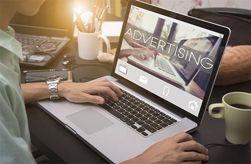 A man works on a laptop. The screen reads “Advertising”.