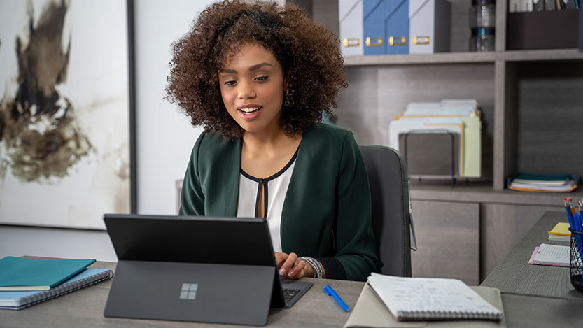 A woman in an office works on a laptop computer while sitting at a desk.