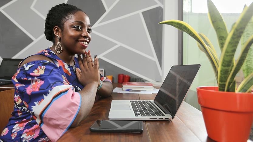 An African-American woman sits at her desk in an office in front of her laptop PC and mobile phone.