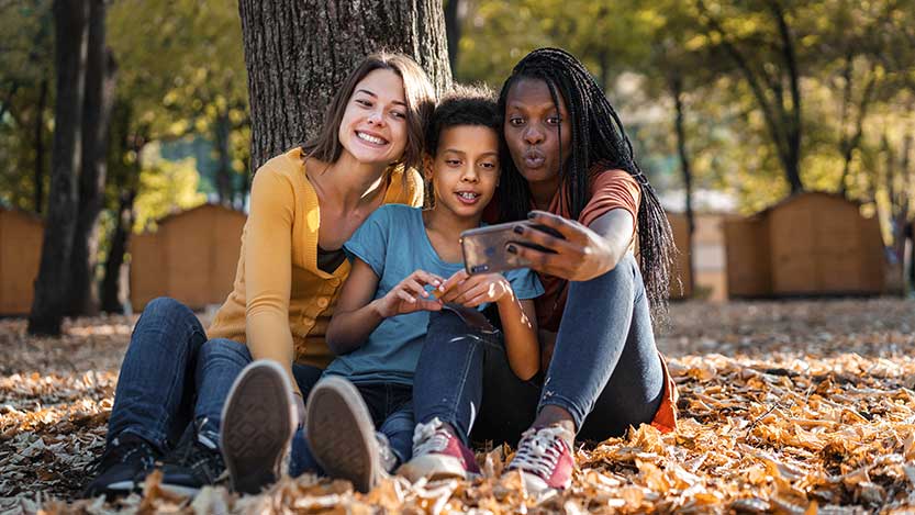 Three youngsters outdoors, taking a picture of themselves with a mobile