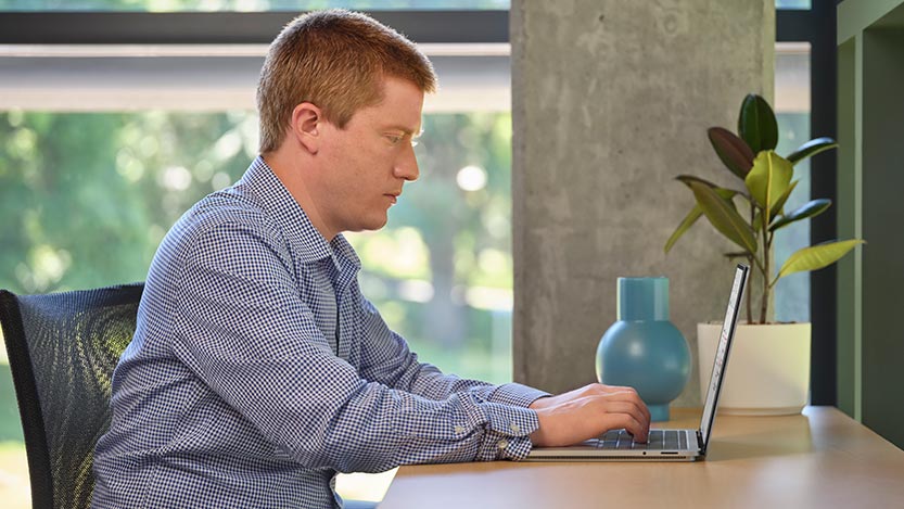 A man sitting at a desk works with a laptop.