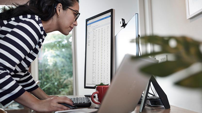 A woman leans over a desktop to be close to a monitor while working on a computer.