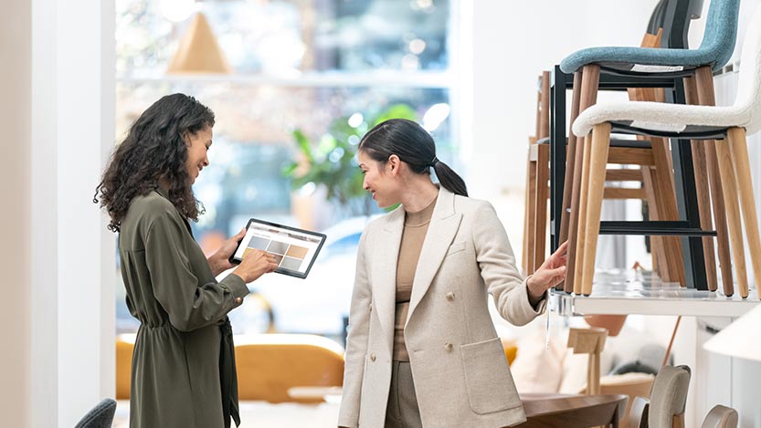 A woman smiles while showing another woman some information on a tablet.