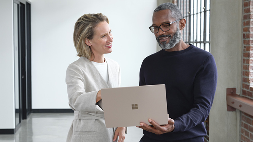 Two people smile as they hold a laptop in front of them.